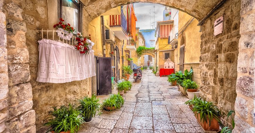 Street of bari vecchia with low arches and plants.
