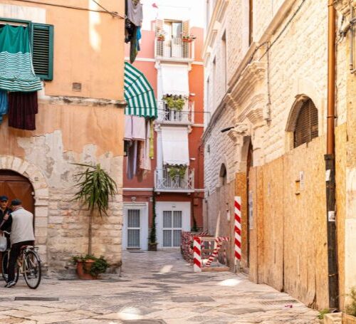 Narrow stone alley in Bari Vecchia with locals and a bike, capturing the charm of cycling in bari